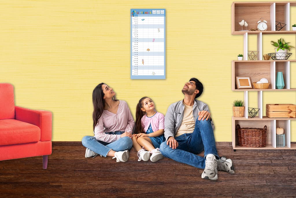 Family sitting on floor looking up at a wall calendar used to coordinate schedules at home